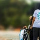 a woman is rolling a person in a wheelchair down a road with trees in the background