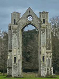 Picture of the ruins of the Priory in Walsingham - looks like a giant stone castle-like arch with lush greenery in the background 